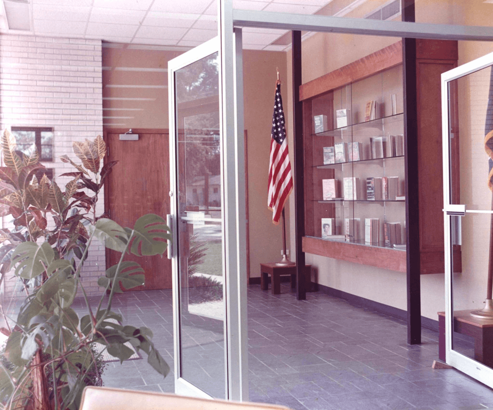 The Pointe Coupee Parish Library entrance with a display of books, potted plants, and the American flag.
