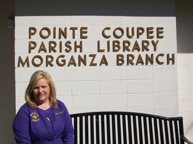 Morganza library branch manager, Dana Bergeron, sitting on a bench in front of Morganza branch sign.