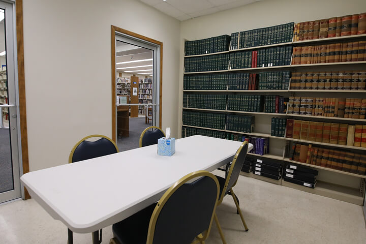 A Pointe Coupee library meeting room in New Roads is furnished with a table, four seats, and a shelf of encyclopedias.