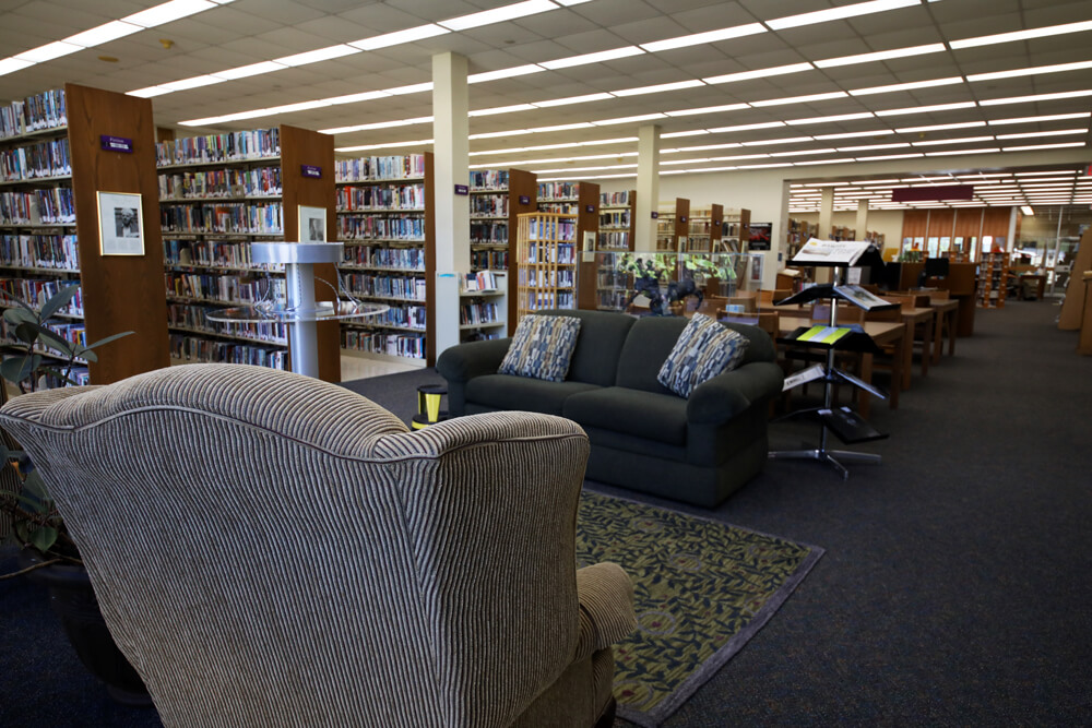 Comfortable sitting area with soft couches, a charging station, and lively plants at Pointe Coupee Parish Library New Roads.
